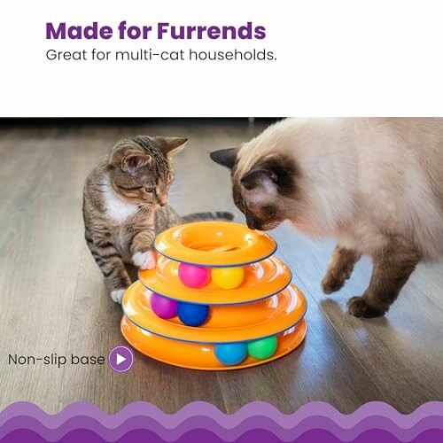 Two cats playing with an orange multi-tiered toy with colorful balls.